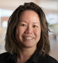 A headshot of Loy who has dark brown hair that goes to the top of her shoulders, brown eyes, and a big smile.